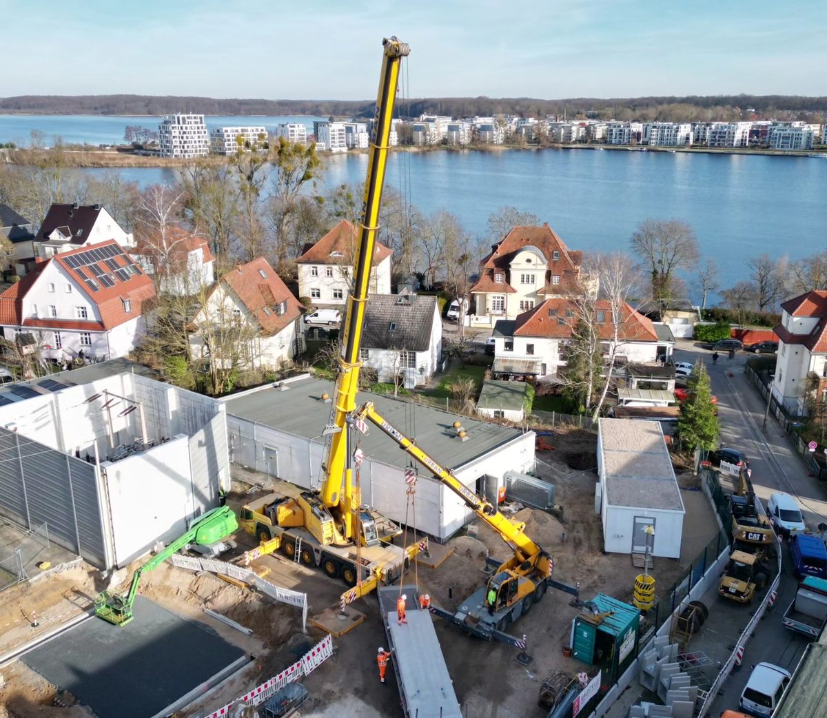 Zwei URBAN-Krane heben gemeinsam ein Betonteil auf einer Baustelle am Wasser